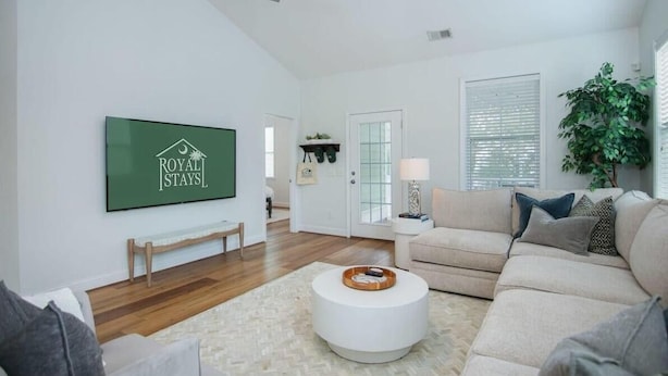 A spacious living room with a large flat-screen TV, a beige sofa, a round coffee table, and a ceiling fan. - The Jade, Park Circle, Mins to Dwtn and Beaches (North Charleston)
