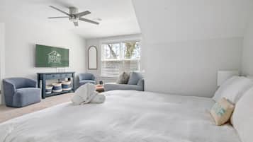A bedroom with a large bed, a ceiling fan, a TV, and a window with blinds.