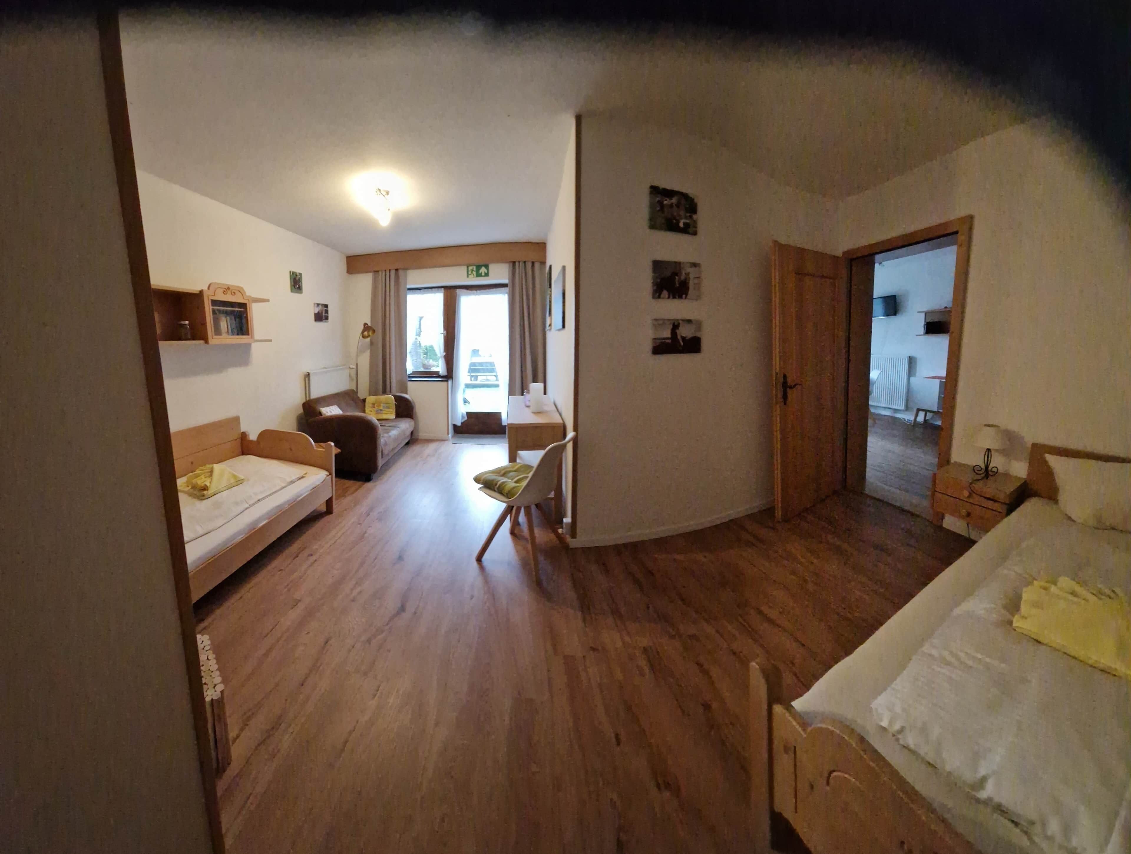 A room with a bed, a sofa, a desk, and a chair. There is a door leading to another room.