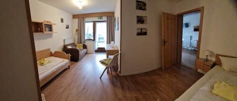 A room with a bed, a sofa, a desk, and a chair. There is a door leading to another room.