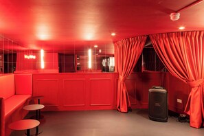 A red-themed room with a sofa, two small tables, a large speaker, and curtains. - Maison Glamsterdam | Amsterdam's Most Unique Stay (Amsterdam)