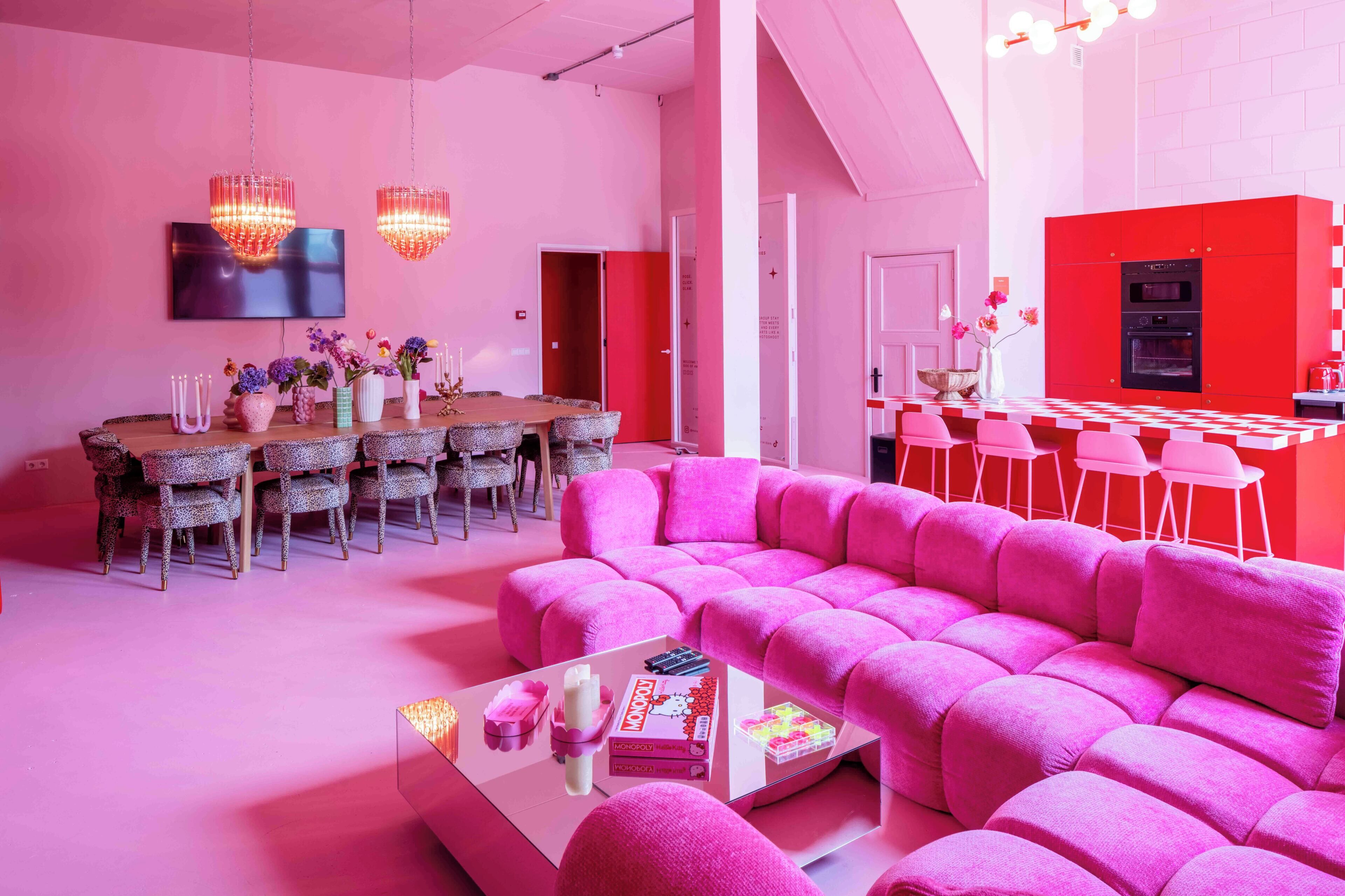 A modern living room with a pink sofa, a dining area with a round table, and a kitchen with red cabinets.