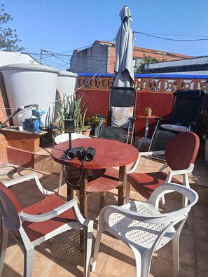 Un patio al aire libre con una mesa redonda, sillas y una parrilla.