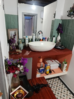 Un baño con un lavamanos grande blanco, baldosas verdes, un espejo y varios artículos de aseo en la encimera.