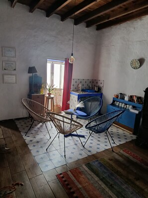 Una habitación con una mesa de comedor, sillas, una zona de cocina y un techo con vigas a la vista.