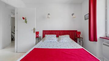 Une chambre à coucher avec un lit, deux tables de chevet, une tête de lit rouge et une fenêtre avec des rideaux rouges.