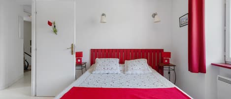A bedroom with a bed, two bedside tables, a red headboard, and a window with red curtains.