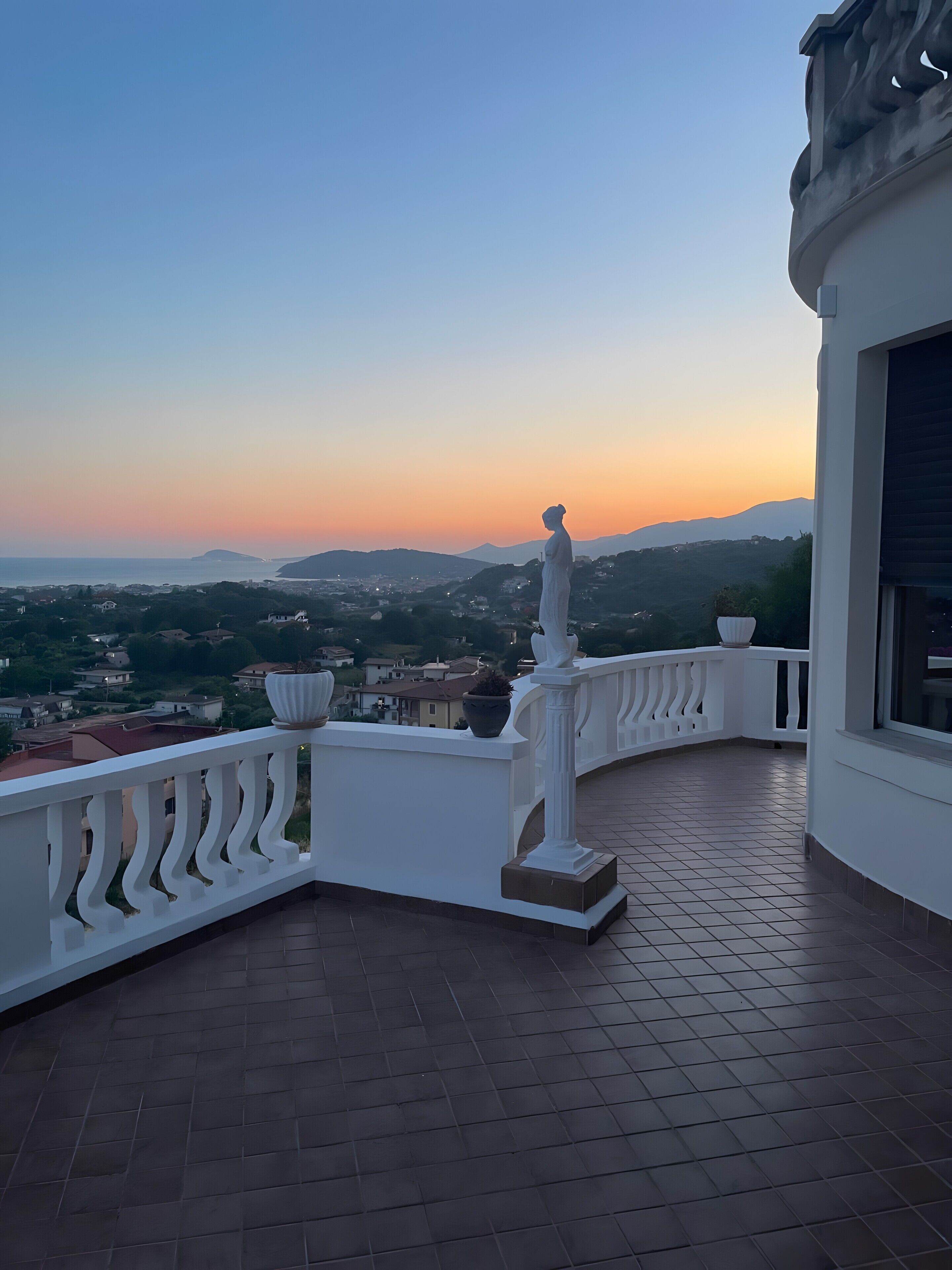 Ein Balkon mit Blick auf einen Sonnenuntergang über einer hügeligen Landschaft.