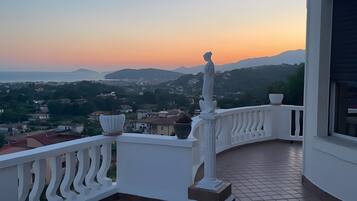 Ein Balkon mit Blick auf einen Sonnenuntergang über einer hügeligen Landschaft.
