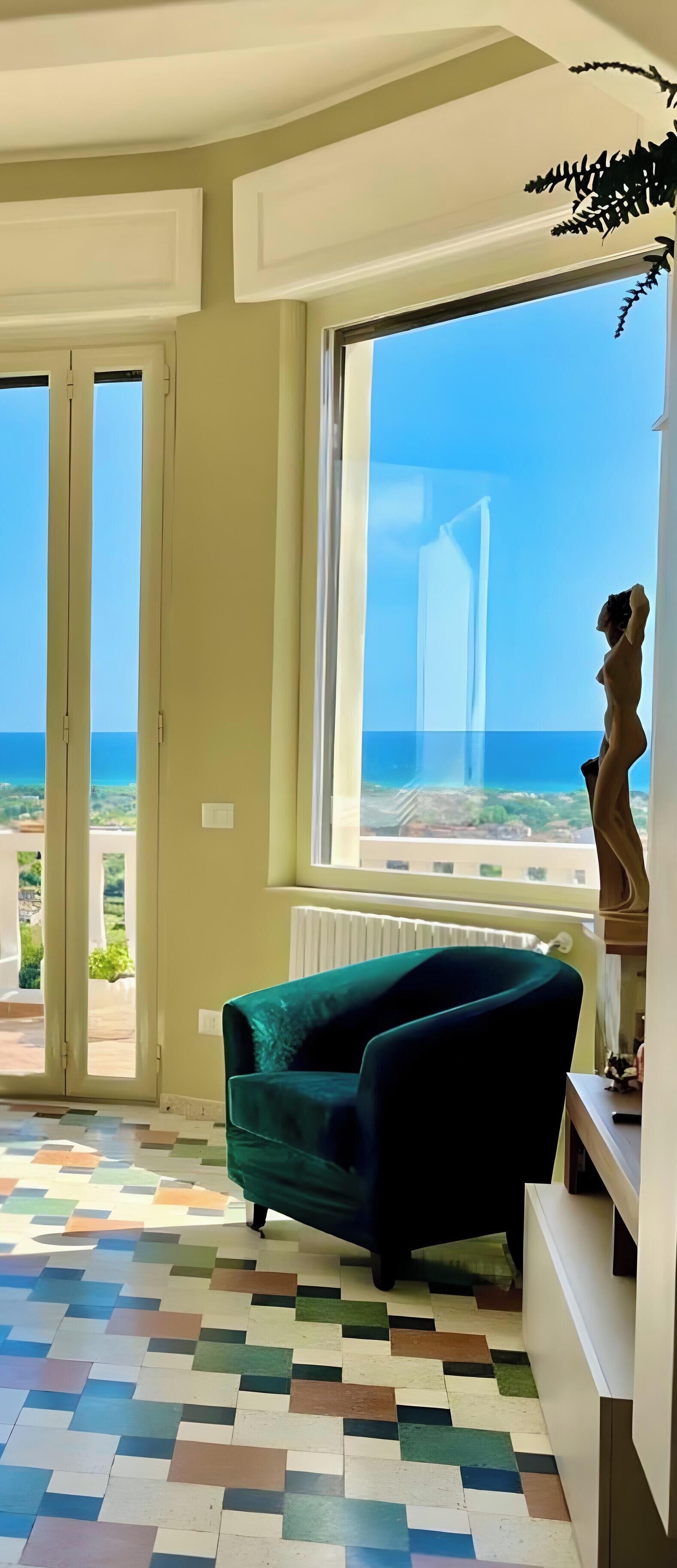 A room with a view of the ocean, a patterned floor, and a green armchair.