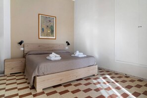 A bedroom with a bed, two bedside tables, a wall-mounted lamp, and a framed artwork.