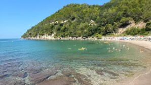 Una platja amb aigua cristal·lina, costa rocosa i un turó boscós al fons.