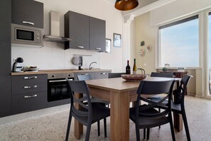 A modern kitchen with a dining area, featuring a large window, a built-in oven, and a wine bottle on the table.