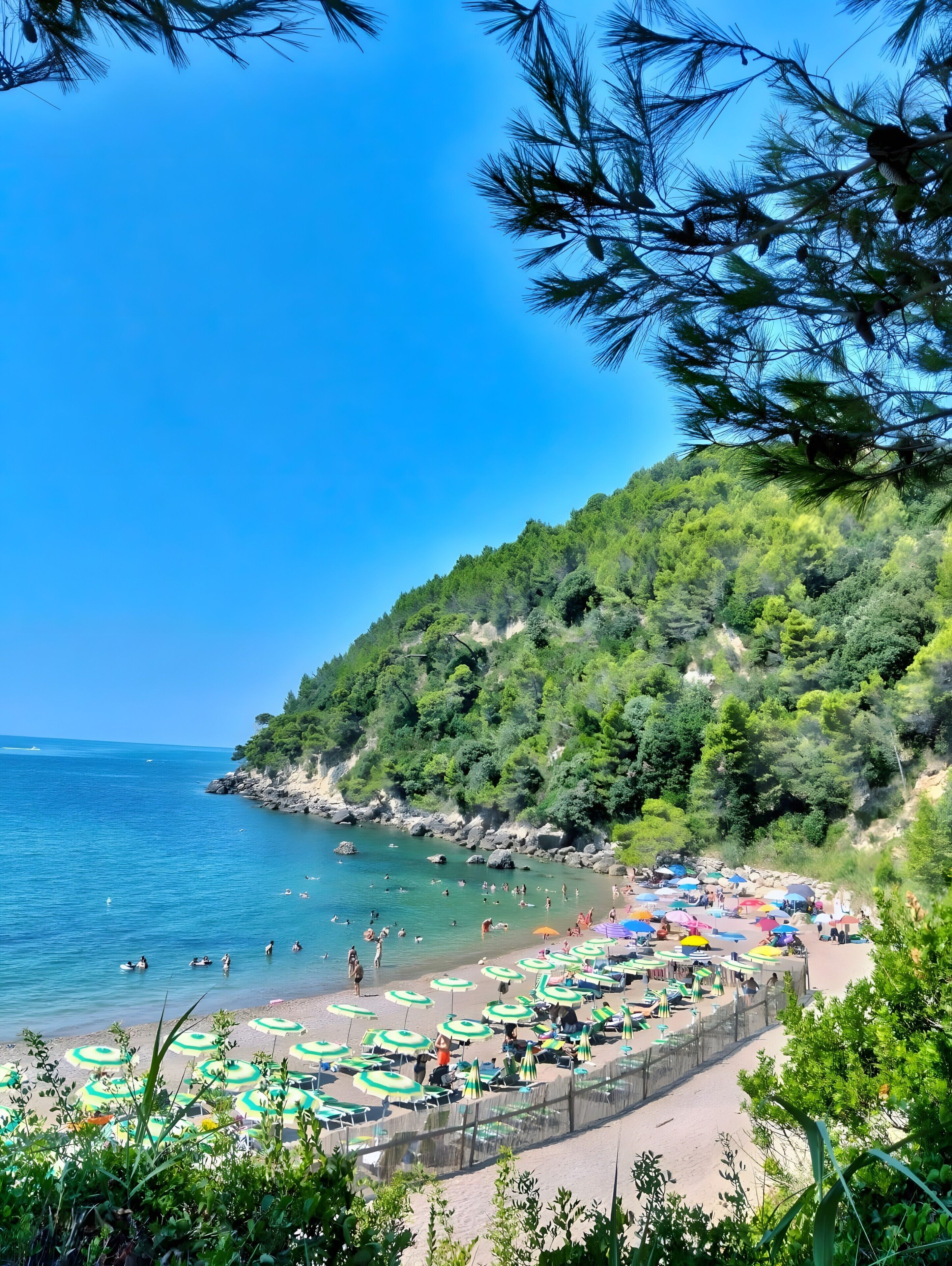 Una spiaggia con ombrelloni e persone, immersa nel verde e sotto un cielo sereno.