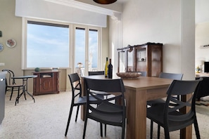 A dining area with a wooden table and chairs, a cabinet, and a view of the sky through large windows.