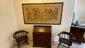 A room with a large framed artwork on the wall, a wooden dresser, and two wooden chairs.
