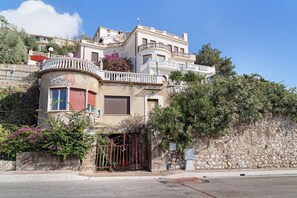 Un edificio de varios pisos con balcones, una pared de piedra y vegetación.