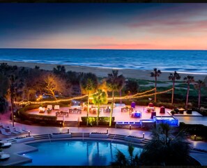 Zona de piscina en un resort con vistas al océano y al atardecer.