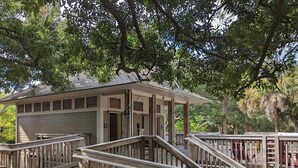 Une terrasse en bois avec des garde-corps, un bâtiment doté d’un toit plat et des arbres environnants.