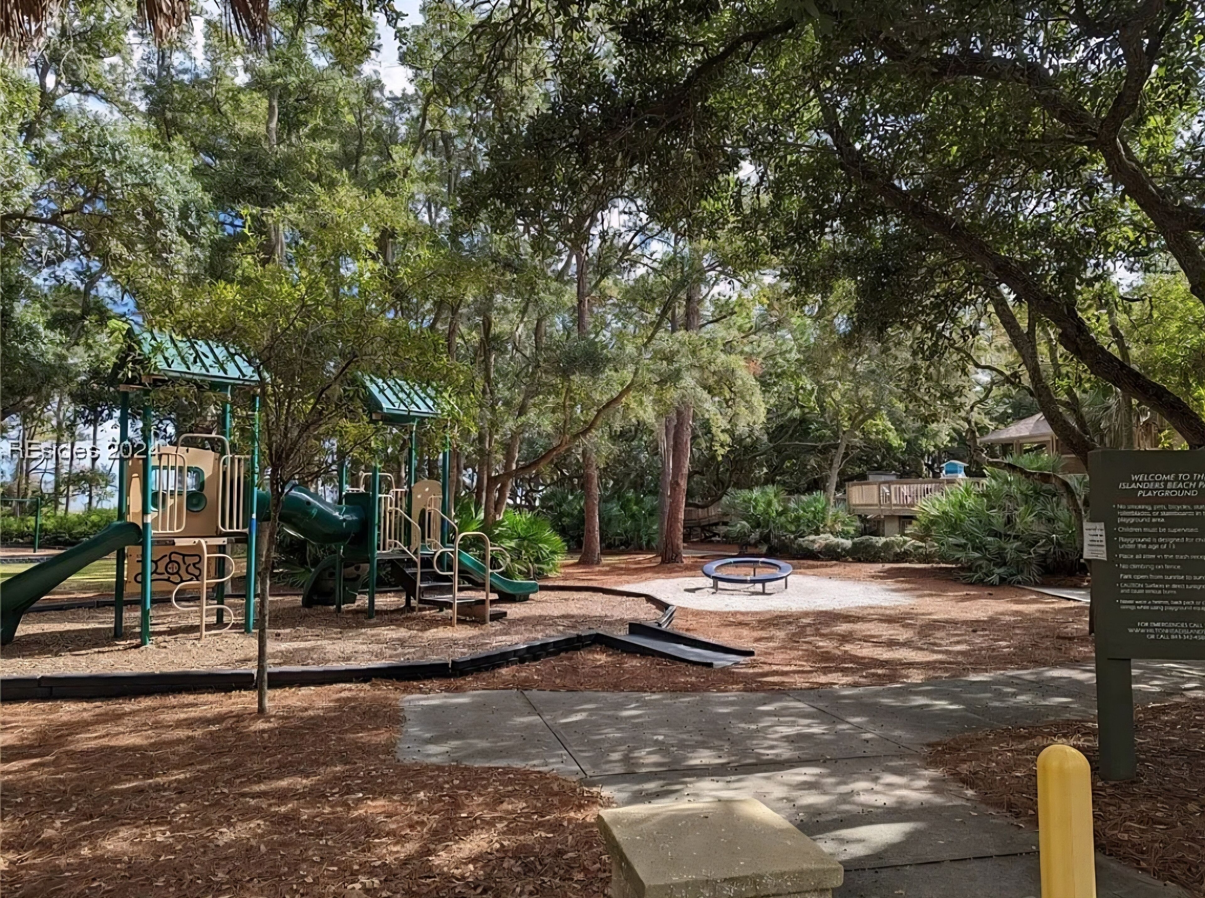 A playground with slides and climbing structures, surrounded by trees.