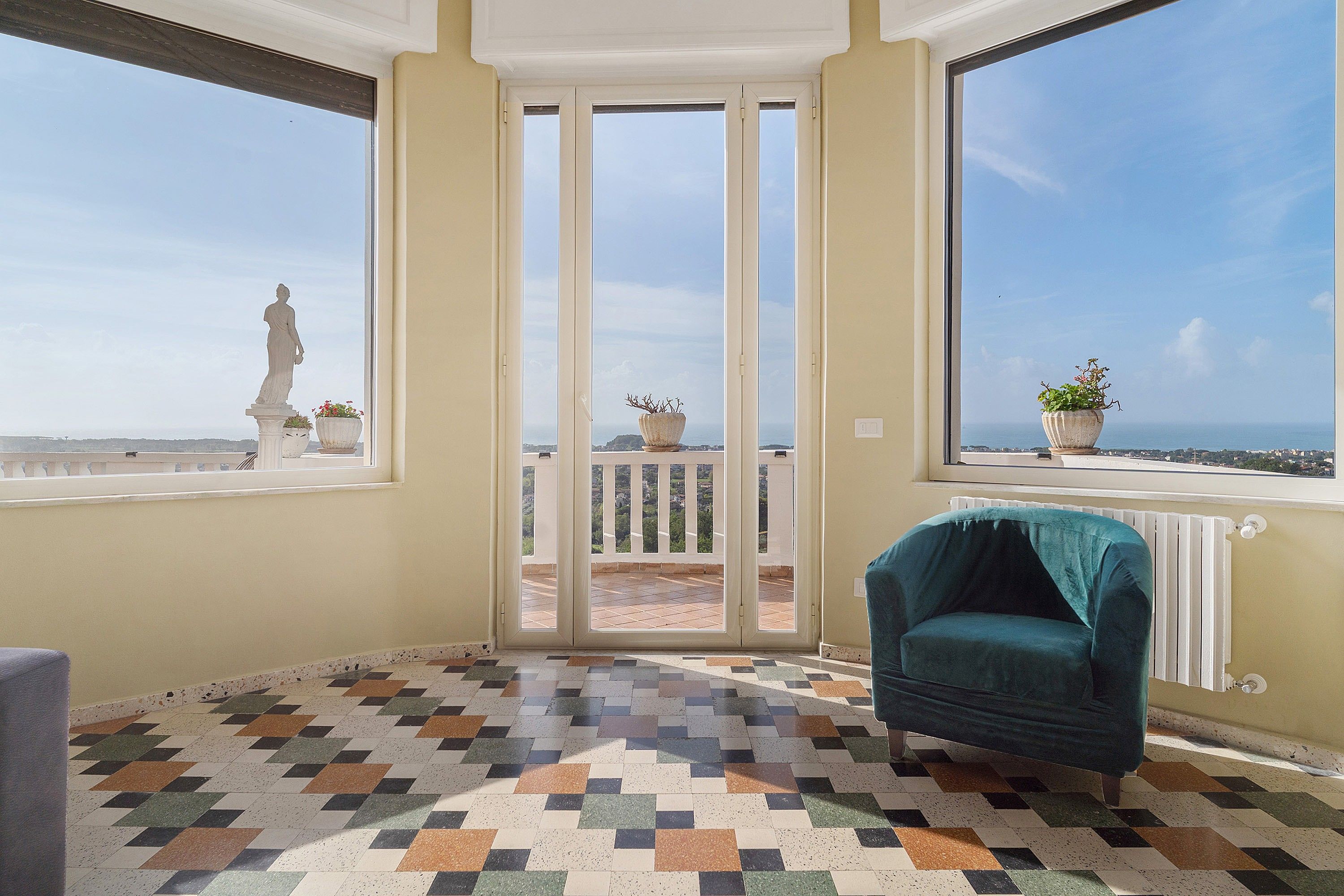 Ein Zimmer mit Fliesenboden, einem Stuhl, einer Statue und Blick durch eine Glastür.