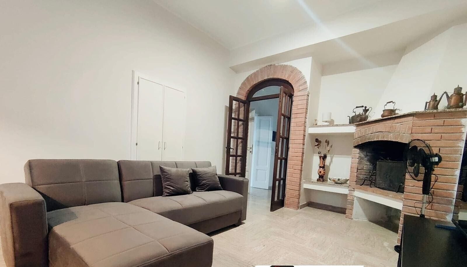 Uma sala de estar com um sofá seccional, uma lareira de tijolos e uma porta branca.