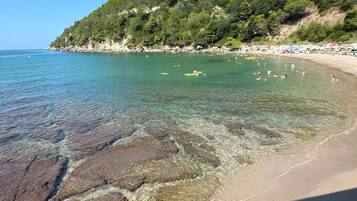 Una playa con aguas cristalinas, costa rocosa y una colina boscosa al fondo.