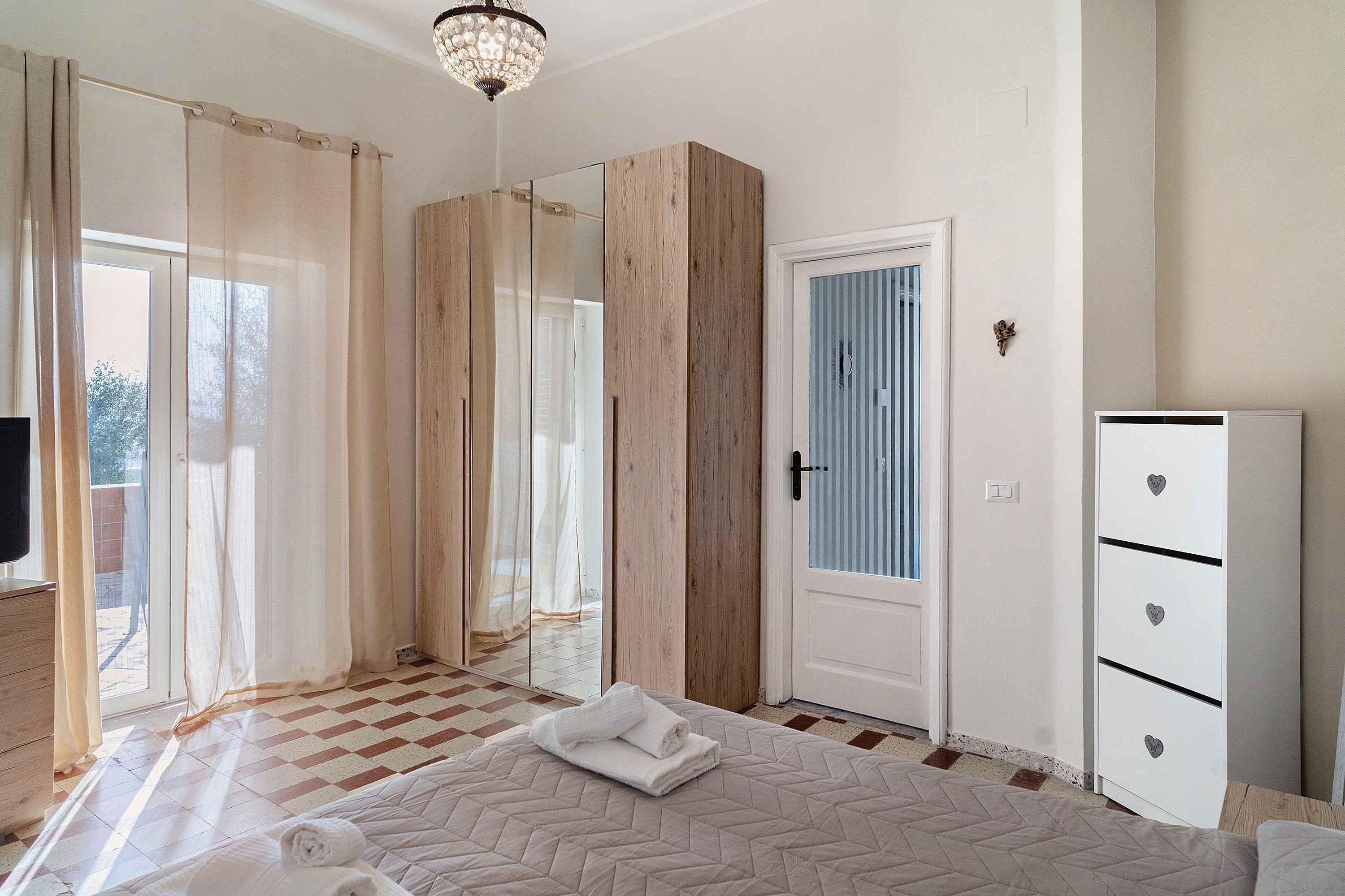 Ein Schlafzimmer mit einem Bett, einem Kleiderschrank, einer Tür mit Fenster und einer Kandelaber.