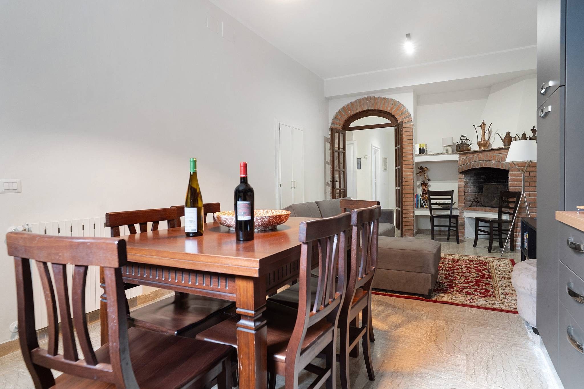 Un comedor con una mesa de madera y sillas, dos botellas de vino y un cuenco de aperitivos.