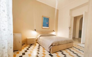 Un dormitori amb llit, taules de nit, una làmpada penjada a la paret, una porta i un terrapatí amb dibuixos.