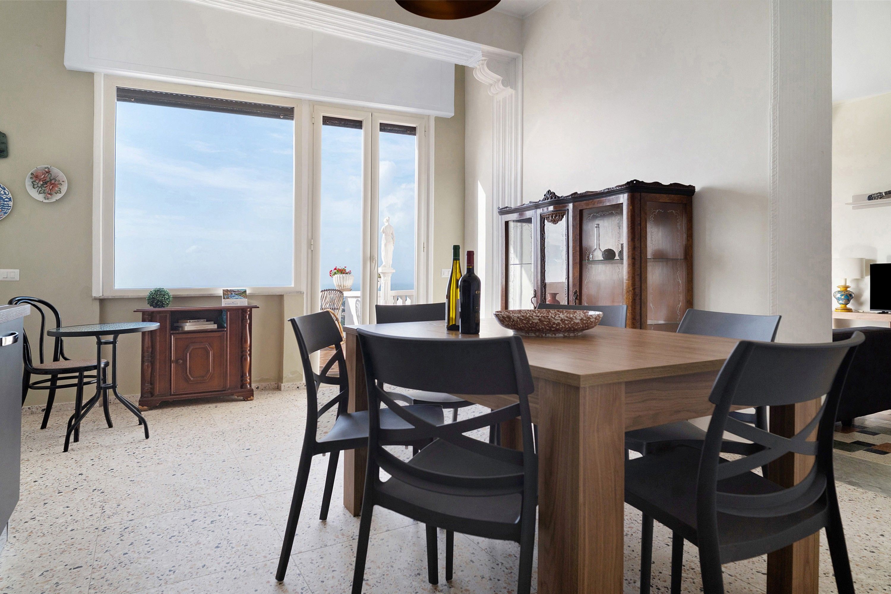 Ein Essbereich mit Holztisch und Stühlen, einer Kommode mit Dekorationsgegenständen und Blick durch große Fenster.