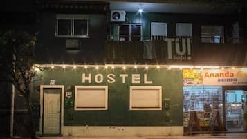 A hostel with a sign reading 'HOSTEL' and a storefront named 'Ananda MINISERVICE' with a contact number.