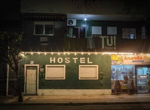 Ostello con un cartello che riporta 'HOSTEL' e una vetrina con l'insegna 'Ananda MINISERVICE' e un numero di telefono.