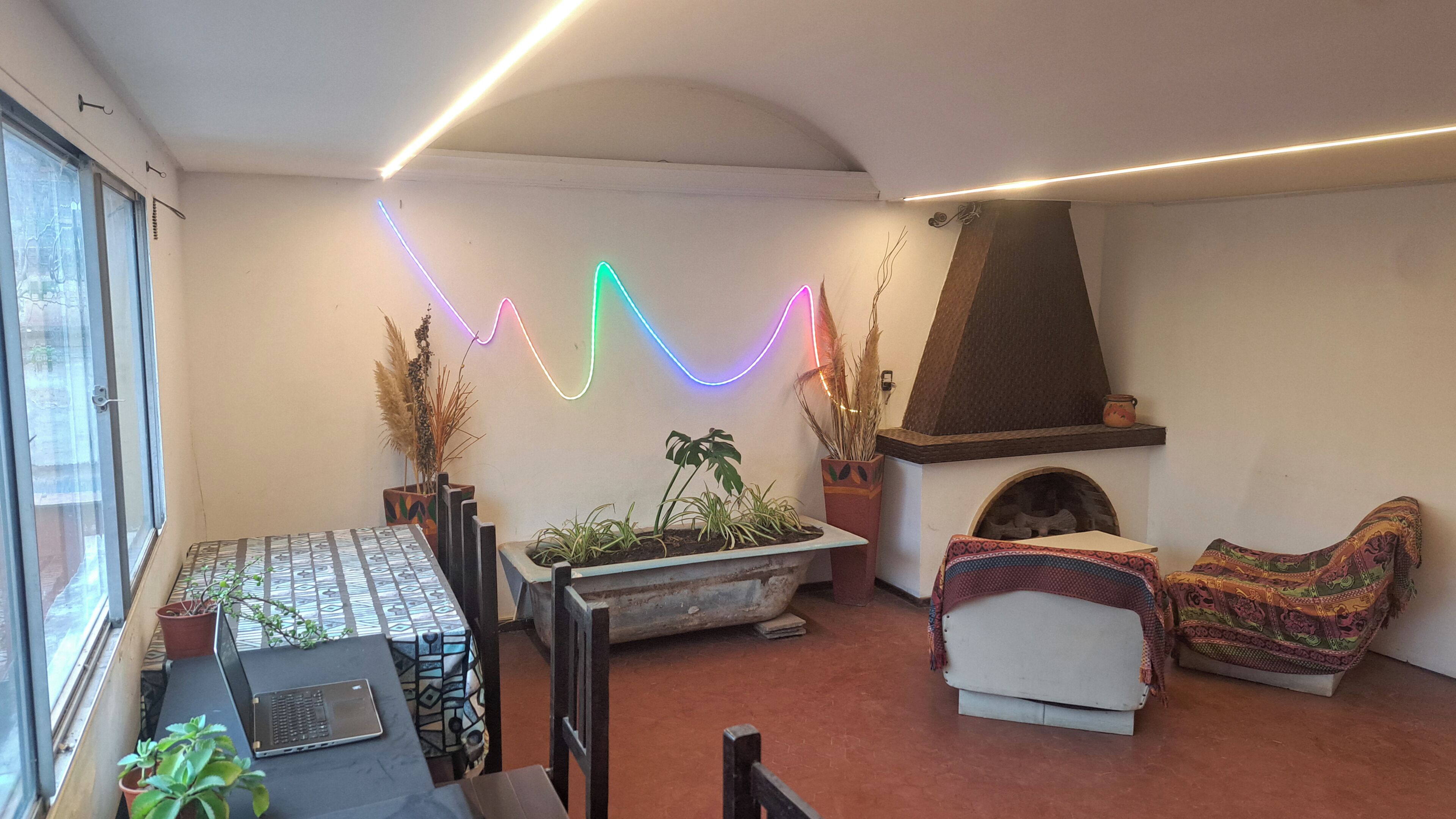A living room with a fireplace, a laptop on a table, and a colorful neon light on the wall.