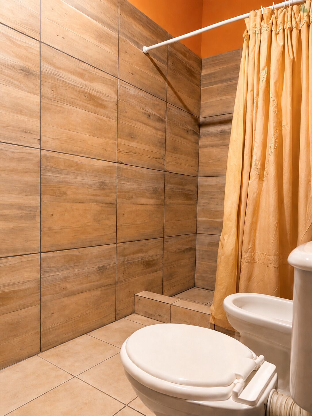 Un baño con azulejos de madera, un inodoro blanco y una cortina de ducha amarilla.