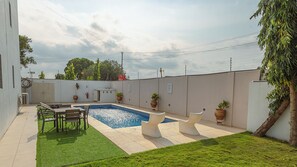 A backyard with a swimming pool, a small patio area with a table and chairs, and potted plants. - Charming 4-bedroom townhome with AC, pool, and Wi-Fi in vibrant East Legon (Accra)