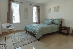 Quarto com cama, cadeira, mesa de cabeceira, abajur e janela.
