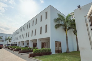 A modern building with multiple windows, a covered walkway, and palm trees. - Charming 4-bedroom townhome with AC, pool, and Wi-Fi in vibrant East Legon (Accra)