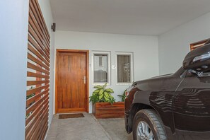 A residential entrance with a wooden door, a vehicle parked to the right, and a potted plant near the door. - Charming 4-bedroom townhome with AC, pool, and Wi-Fi in vibrant East Legon (Accra)