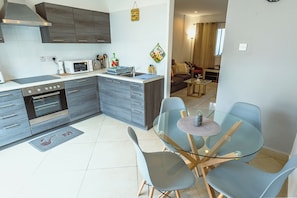 Cozinha moderna com armários cinza, micro-ondas e pia. Há uma área de refeições com mesa de vidro e cadeiras.