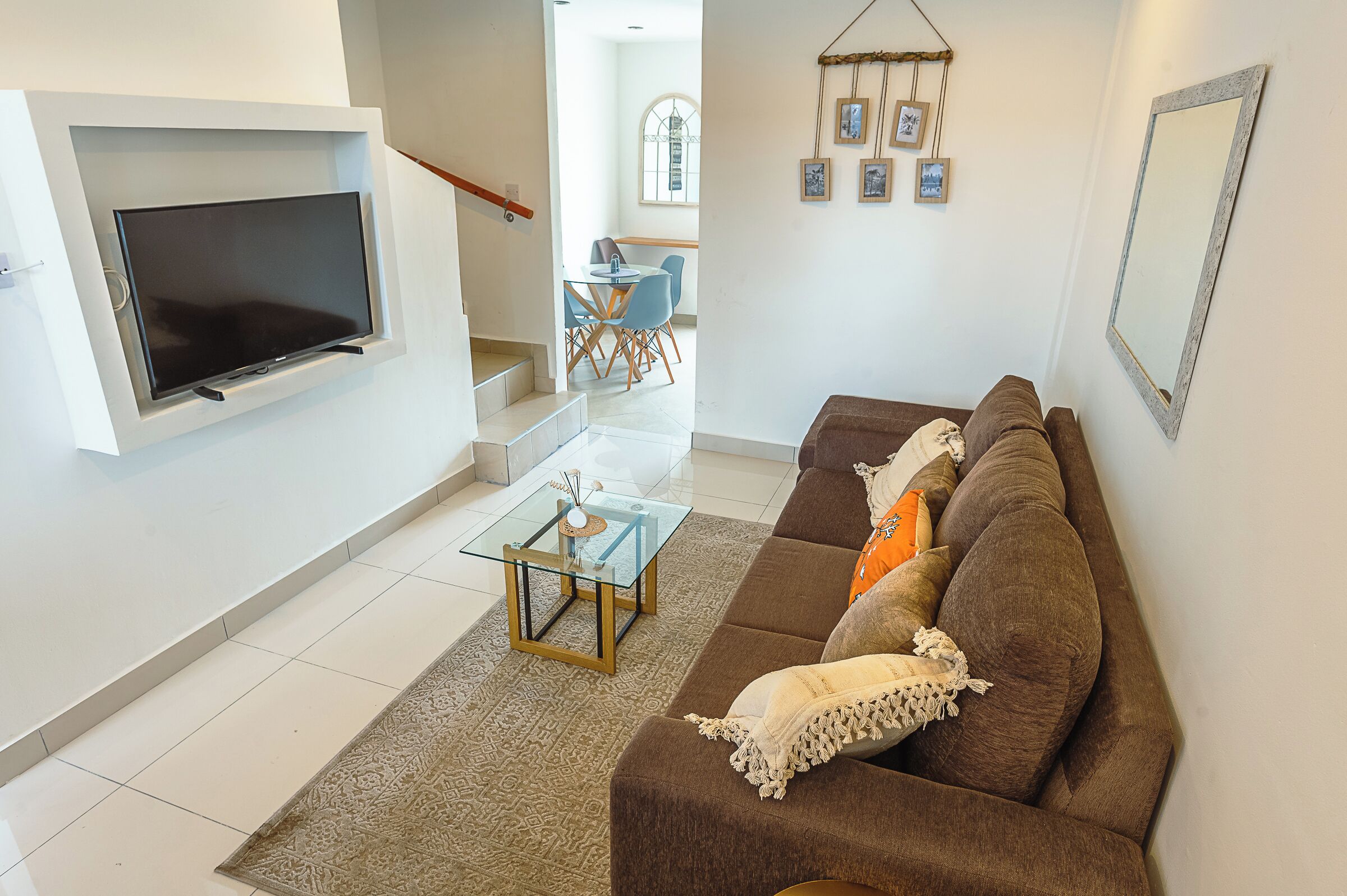 A living room with a TV, sofa, coffee table, and a dining area in the background.