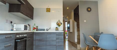 A modern kitchen with dark wood cabinets, a built-in oven, and a microwave. There is a dining area with a table and chairs, and a hanging light fixture.