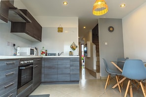 Una cocina moderna con armarios de madera oscura, horno empotrado y microondas. Cuenta con un área de comedor con mesa y sillas, y una lámpara colgante.