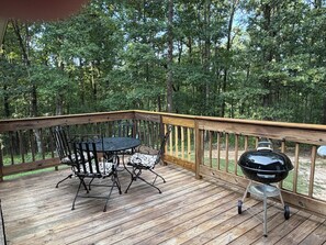 A wooden deck with a table and chairs, a barbecue grill, and a view of a forest.