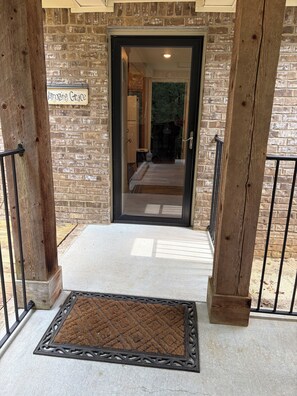 A wooden door with a glass panel, a sign above it, and a doormat in front.