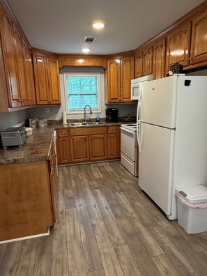 A kitchen with wooden cabinets, a white refrigerator, a sink, and a window with blinds.