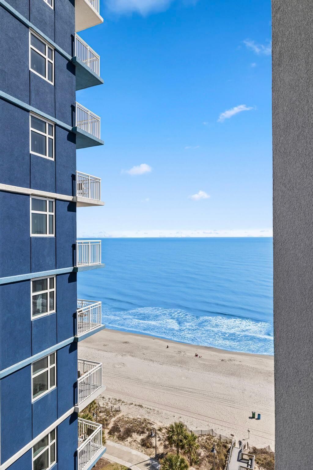 A high-rise building with multiple balconies overlooking a beach and ocean.