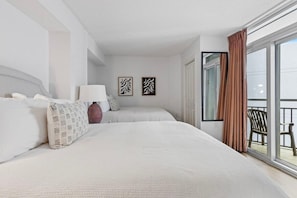 Ett modernt hotellrum med en stor säng, ett nattduksbord, en lampa och två inramade konstverk på väggen.