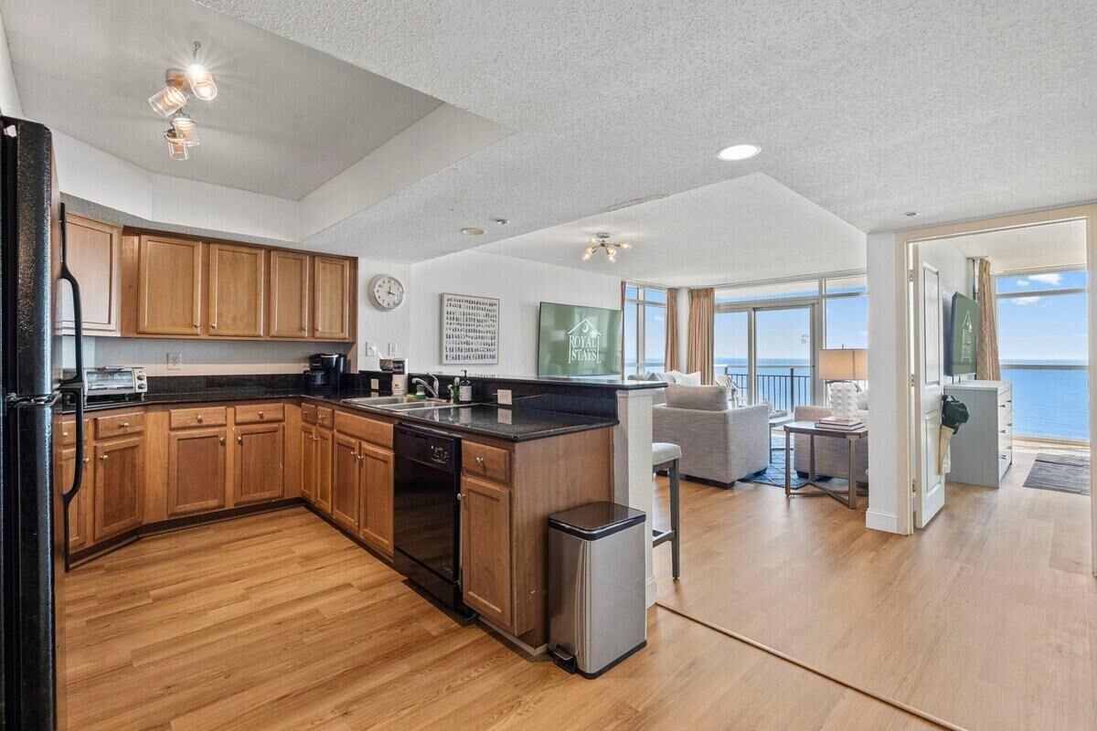 A spacious kitchen with wooden cabinets and a central island, a dining area with a view of the sea, and a living room with a large window.