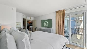 Ein Schlafzimmer mit einem großen Bett, einem an der Wand montierten Fernseher und einer Glastür, die zu einem Außenbereich mit Sitzgelegenheiten führt.